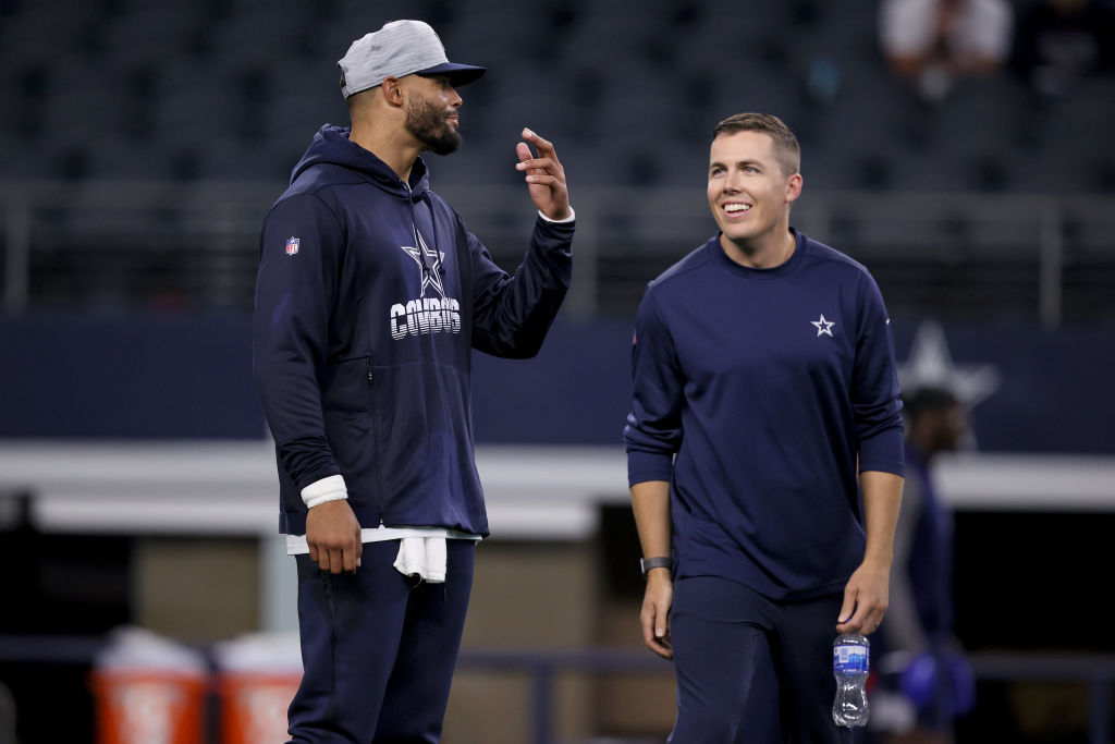 ARLINGTON, TEXAS - AUGUST 21: Quarterback Dak Prescott #4 of the Dallas Cowboys talks with offensive coordinator Kellen Moore of the Dallas Cowboys on the field during pregame warm-ups before the Dallas Cowboys take on the Houston Texans in a preseason NFL game at AT&T Stadium on August 21, 2021 in Arlington, Texas.